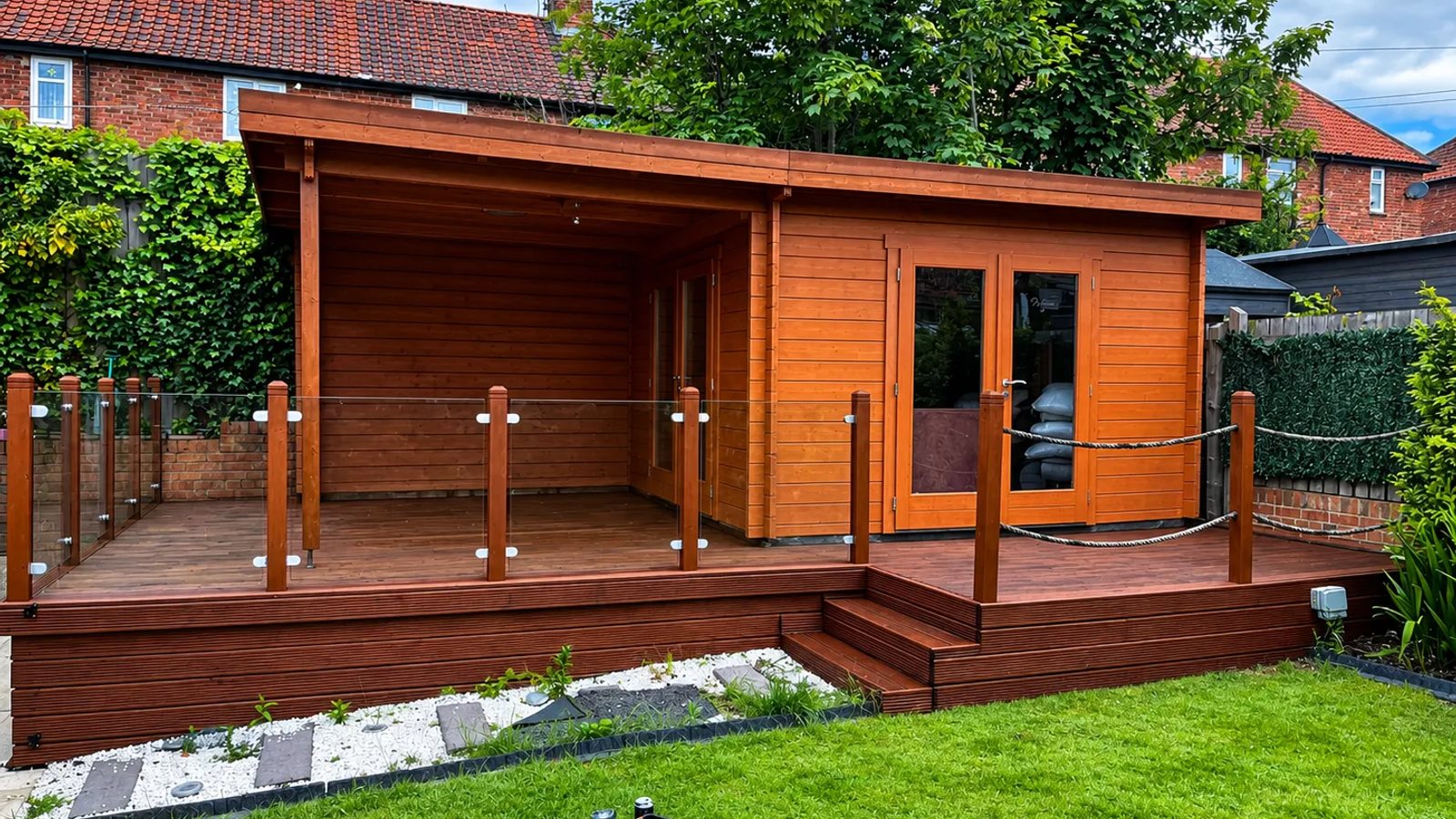 Timber garden room with glass balustrade and raised decking, stained a warm red-brown